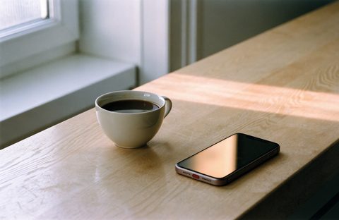 A phone next to a cup of coffee on a kitchen counter, in the first morning sun.