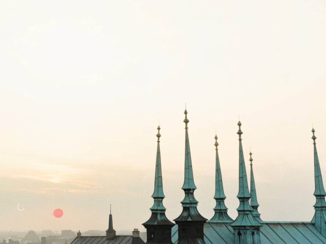 Copenhagen's copper spires against a pale sunrise, a low red sun over the rooftops.